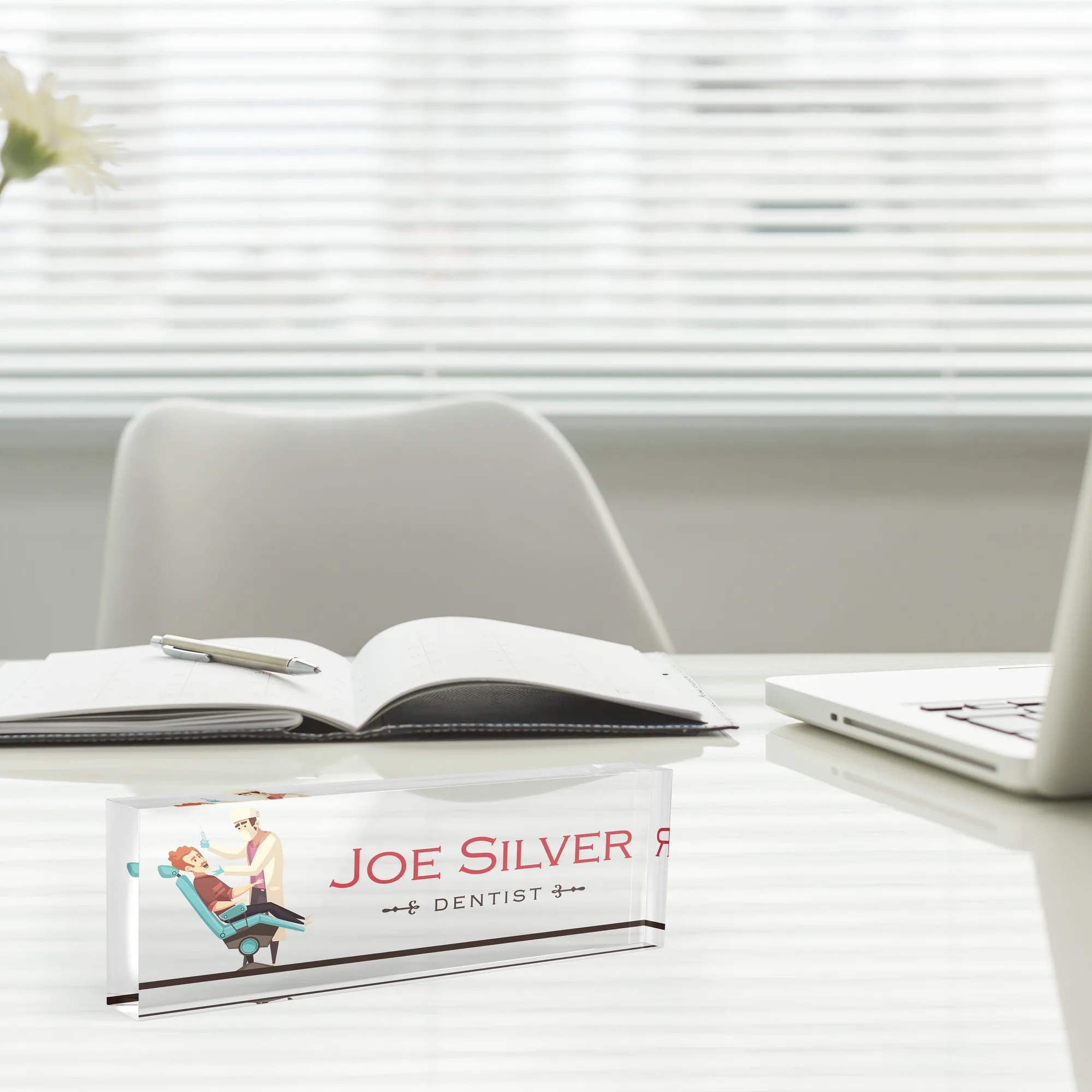 Acrylic desk name plate with a dental practice illustration design beside an open notebook and a laptop