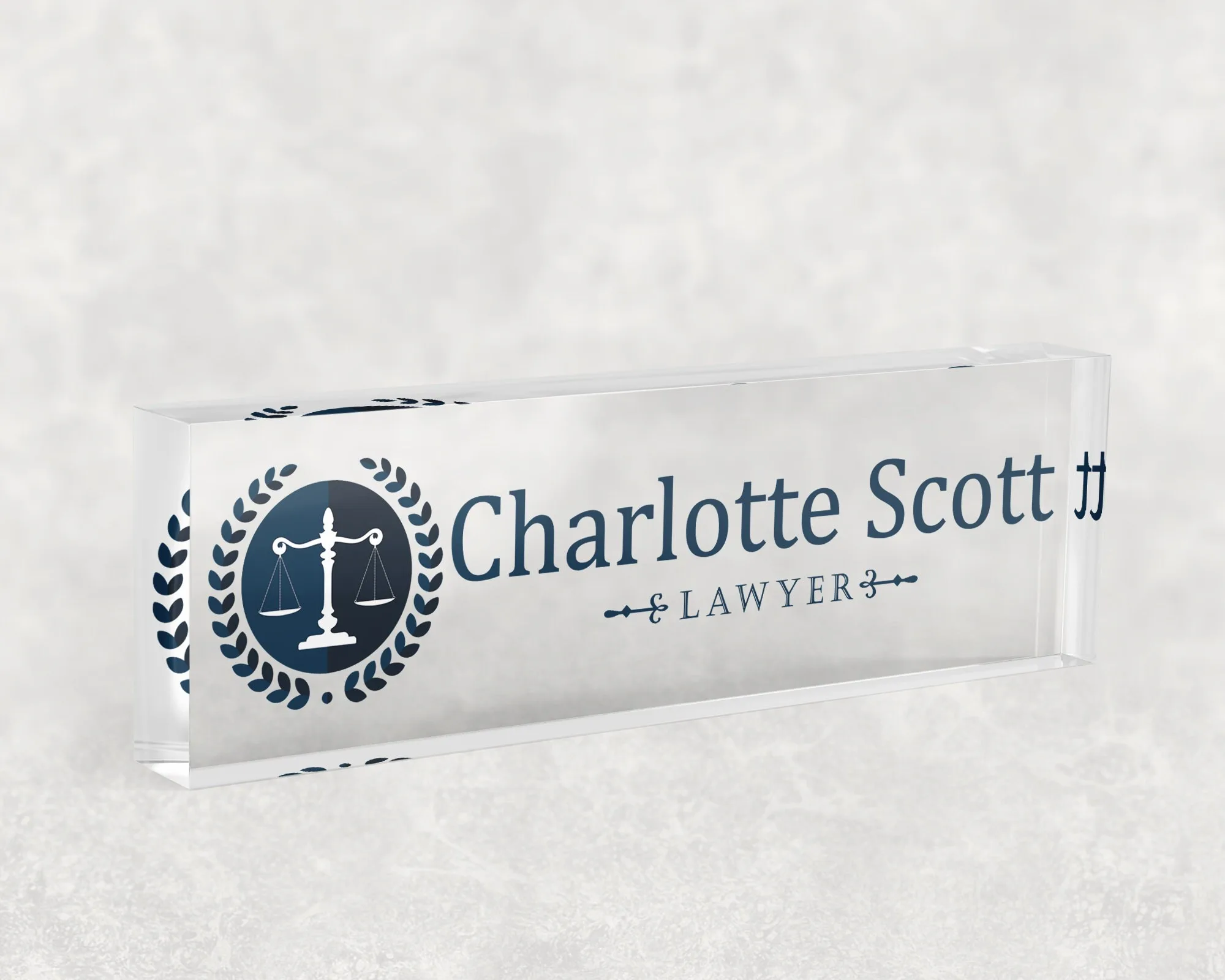 Studio view of a clear acrylic desk name plate with a navy scales of justice design