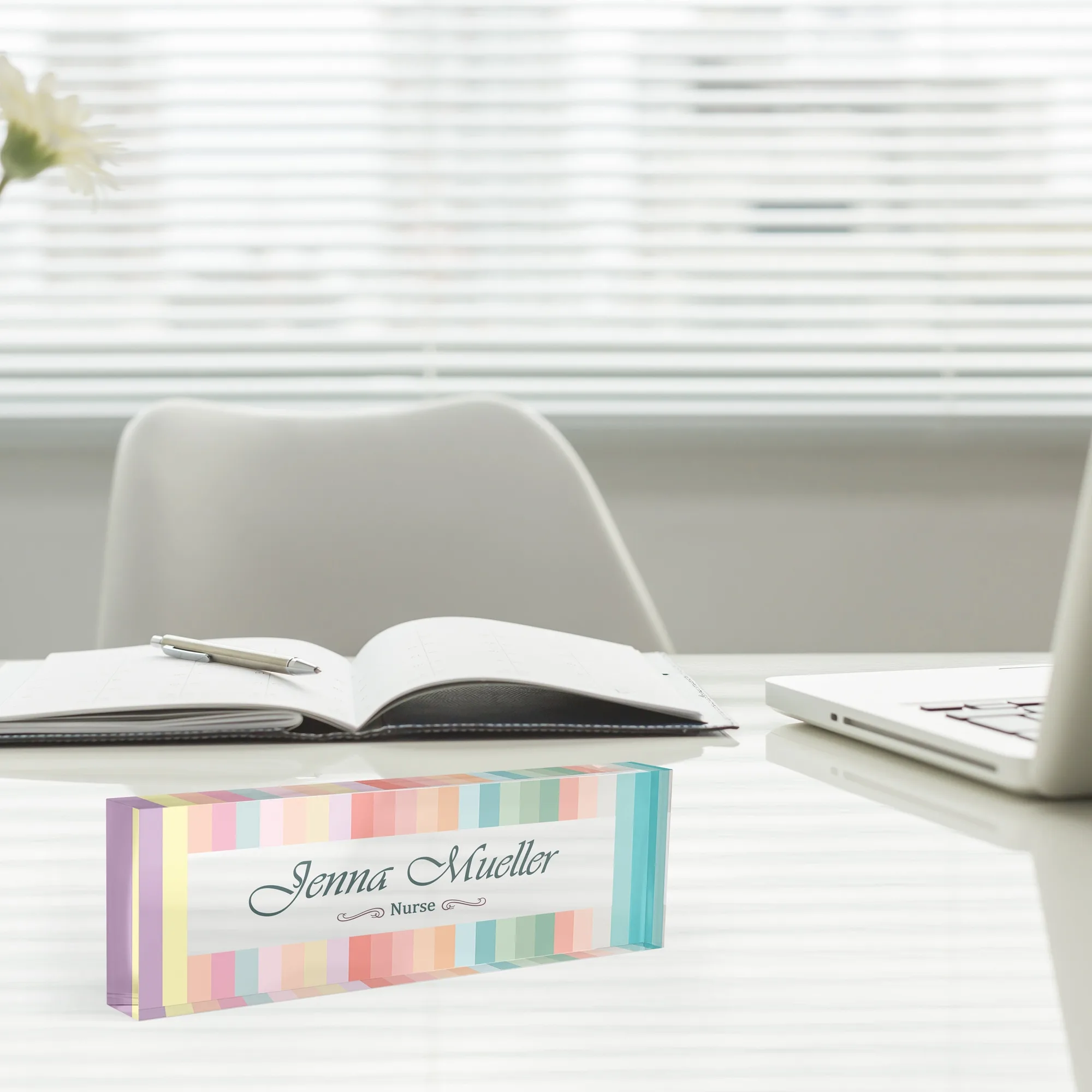 Acrylic desk name plate with a soft pastel stripe design beside an open notebook and a laptop
