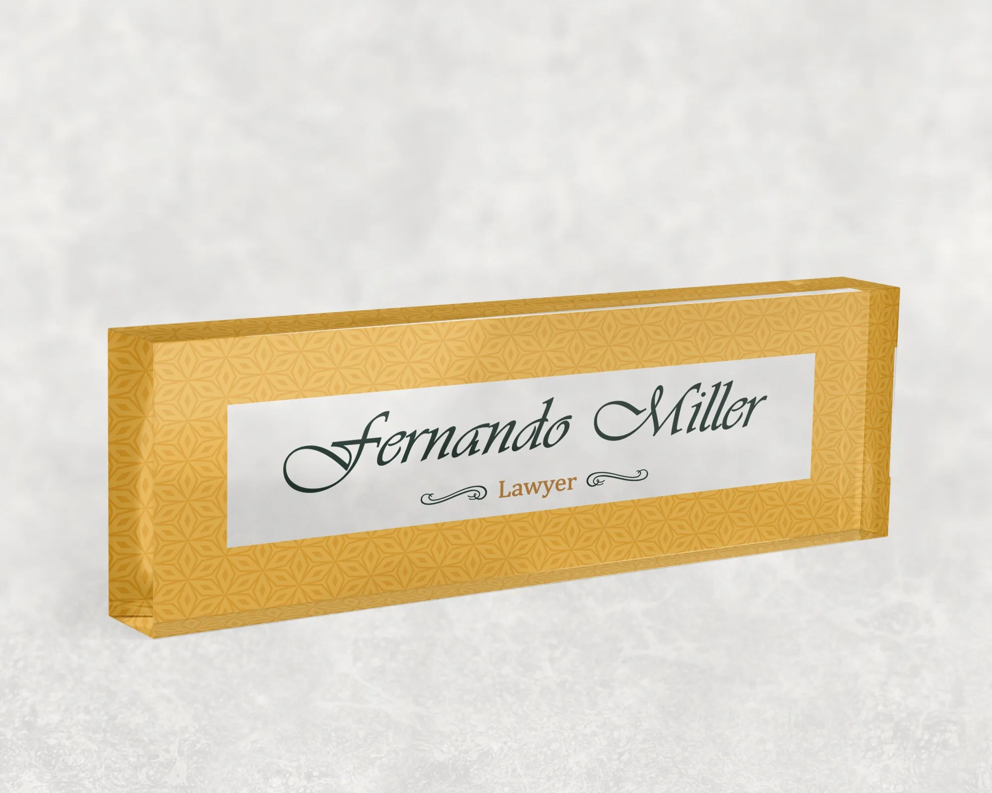 Studio view of a clear acrylic desk name plate with a mustard and gold pattern design