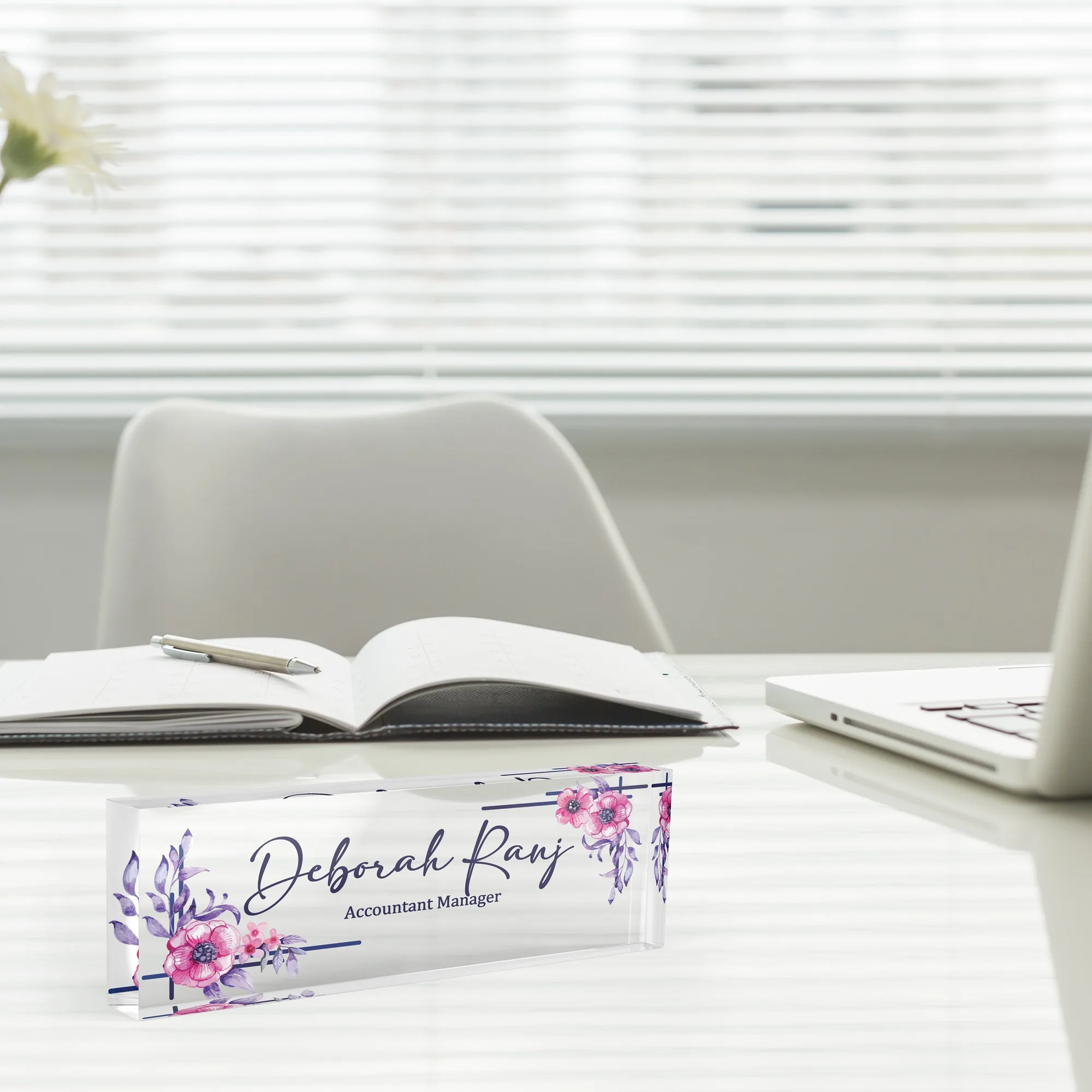 Acrylic desk name plate with a pink rose spray design beside an open notebook and a laptop