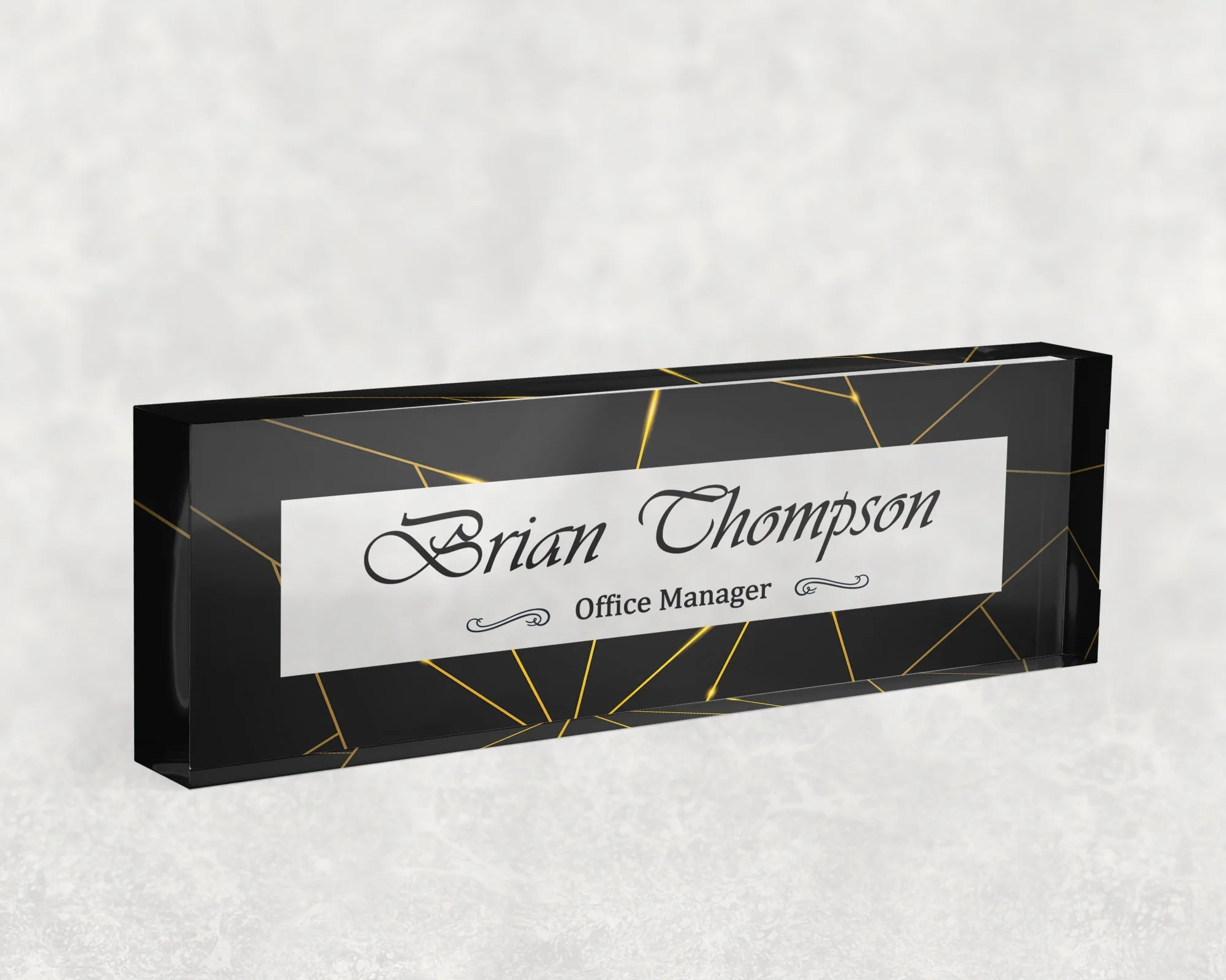 Studio view of a clear acrylic desk name plate with a black and gold line design