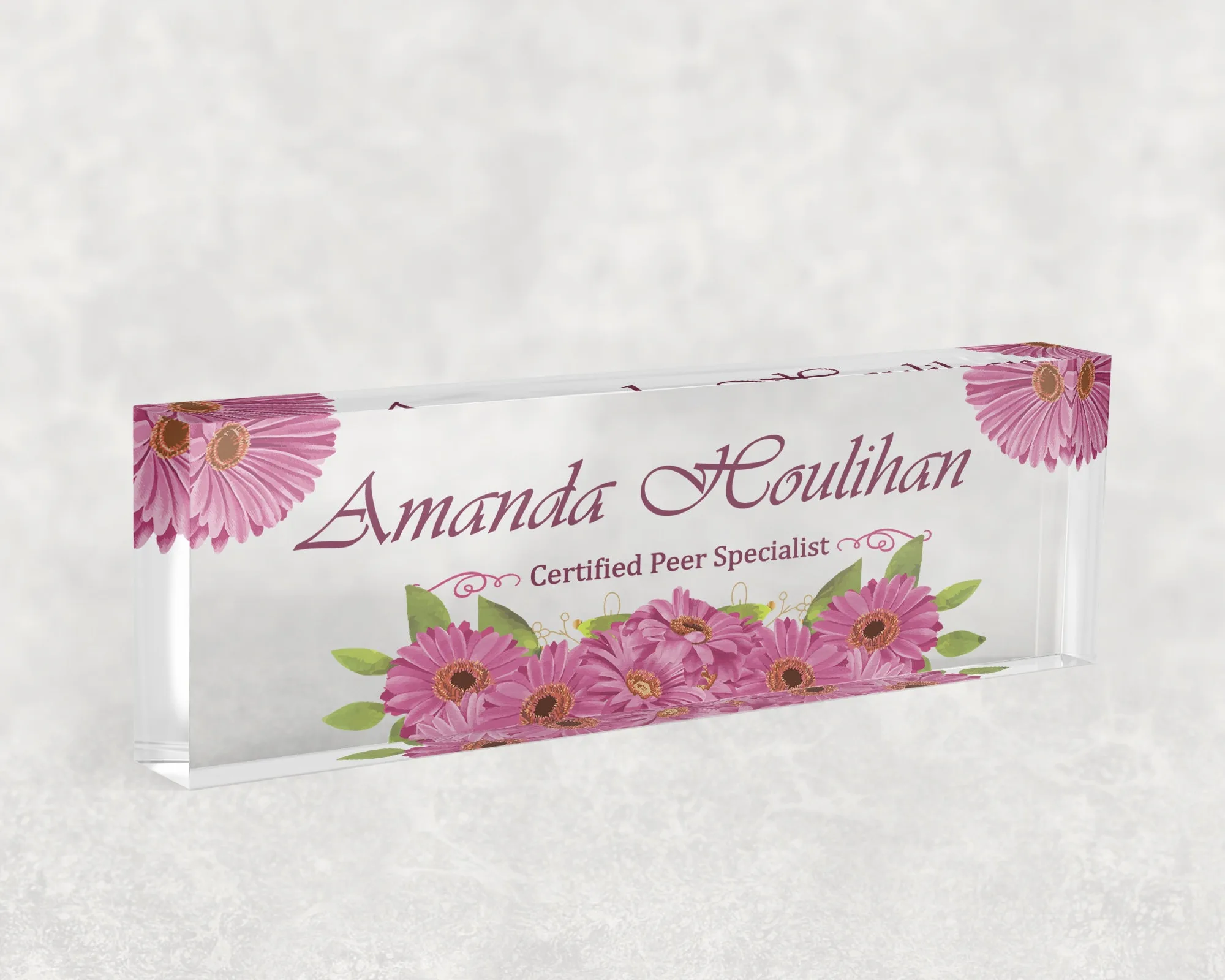 Studio view of a clear acrylic desk name plate with a pink gerbera daisy design
