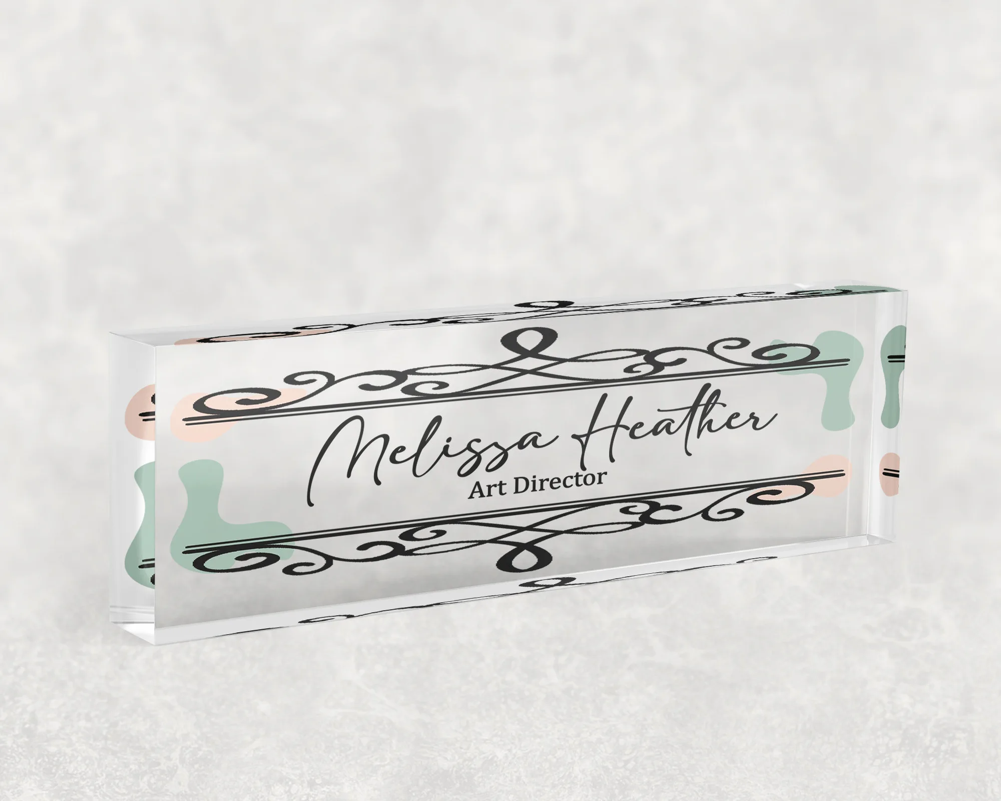 Studio view of a clear acrylic desk name plate with a black scroll and sage wash design