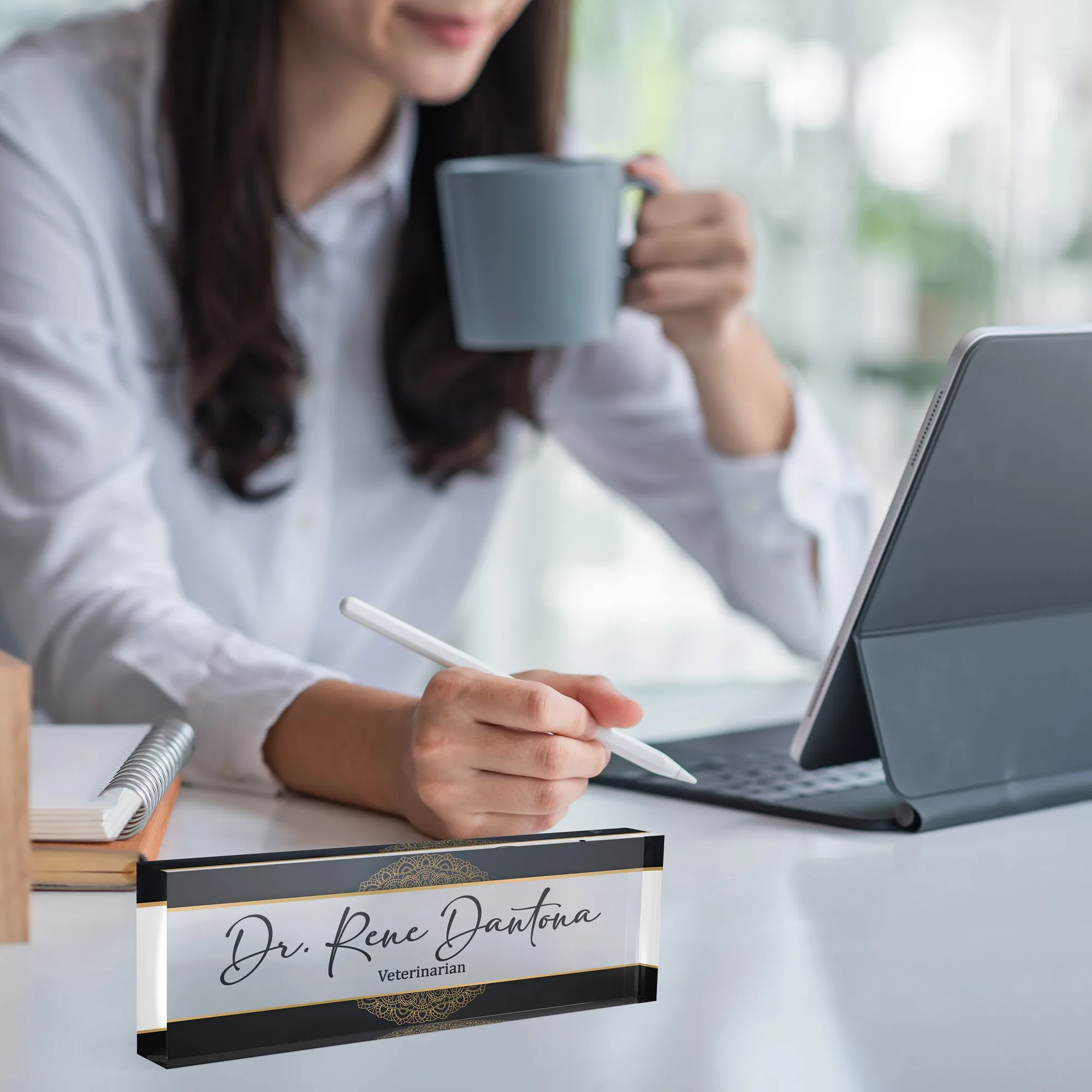 Acrylic desk name plate with a plain black framed design on a white desk beside a tablet and a coffee mug