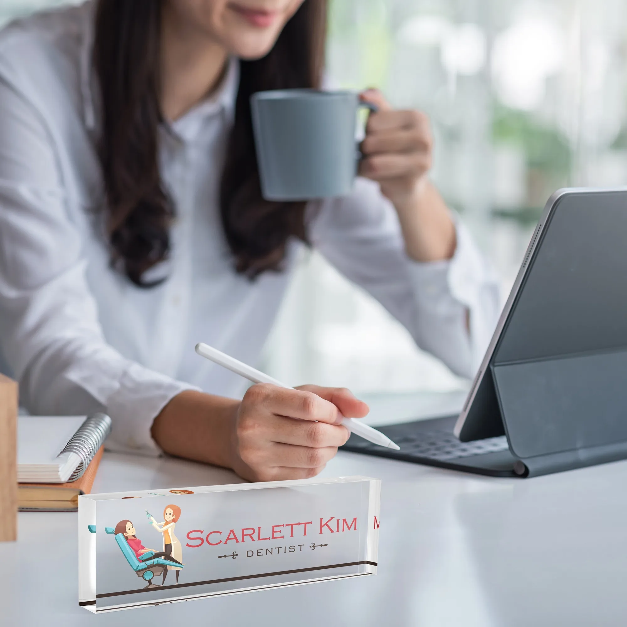Acrylic desk name plate with a dental surgery illustration design on a white desk beside a tablet and a coffee mug
