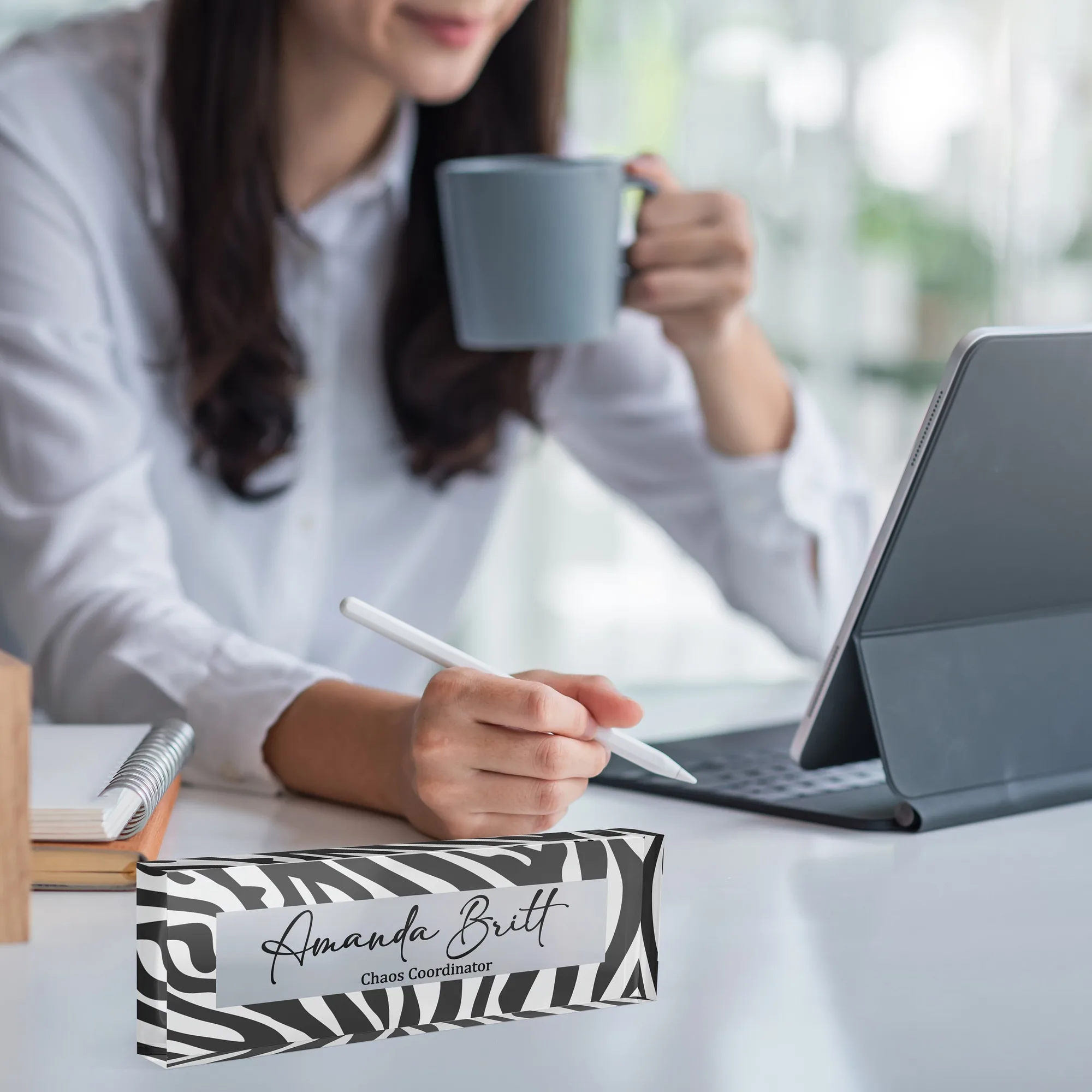 Acrylic desk name plate with a black and white zebra print design on a white desk beside a tablet and a coffee mug