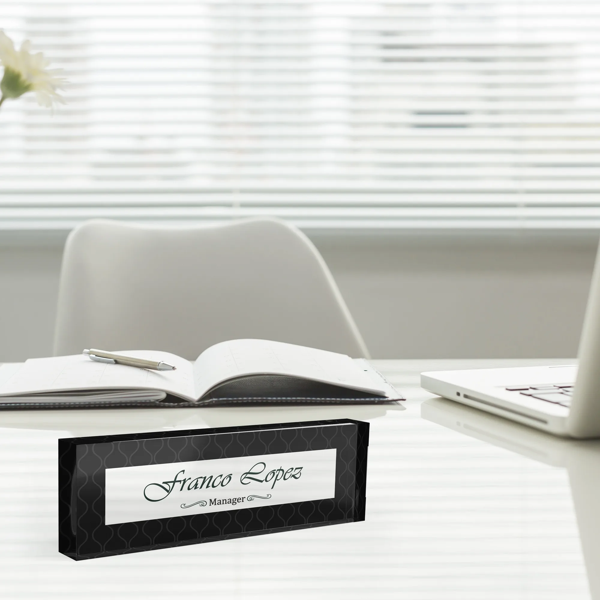Acrylic desk name plate with a black on black damask design beside an open notebook and a laptop