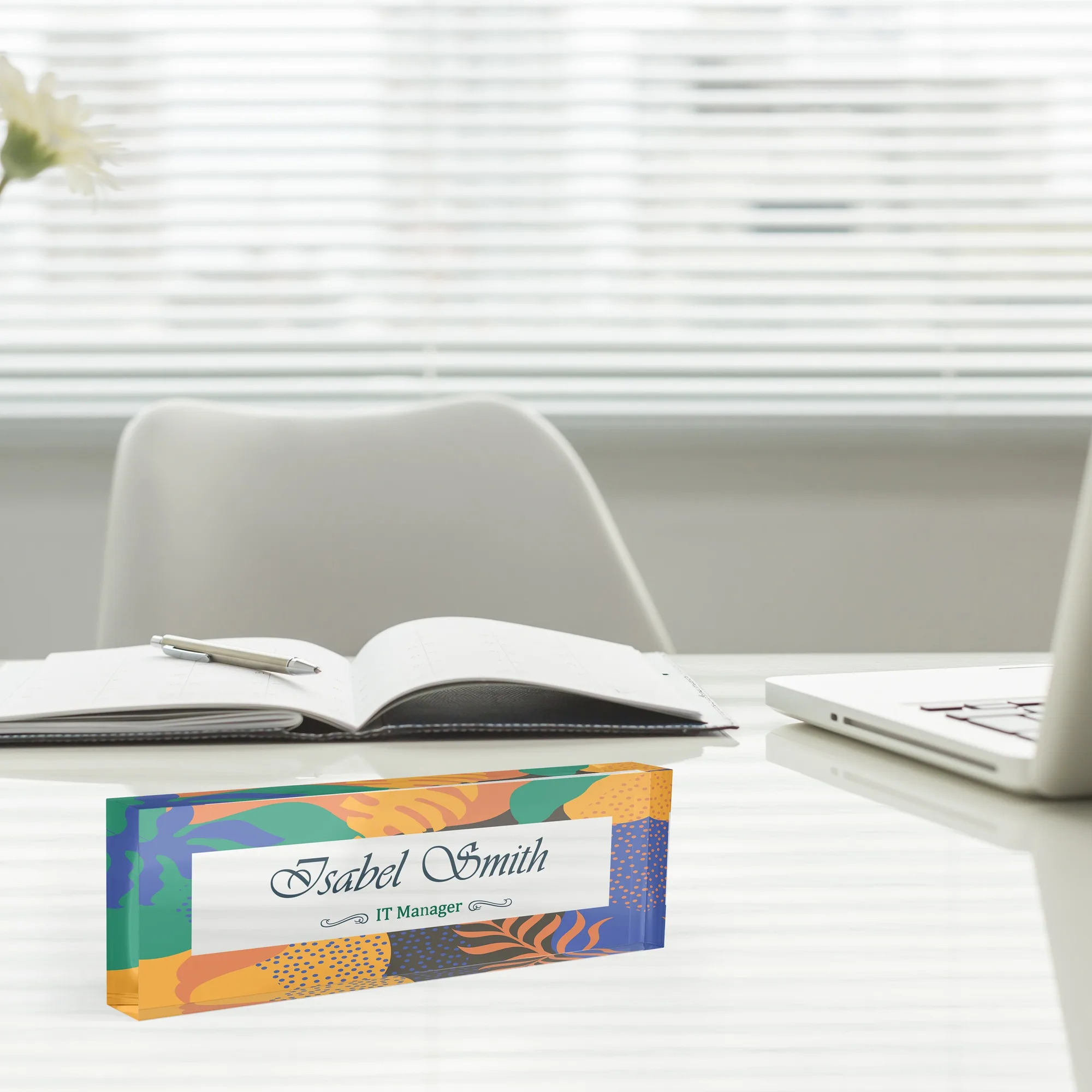 Acrylic desk name plate with an abstract cut shape design beside an open notebook and a laptop