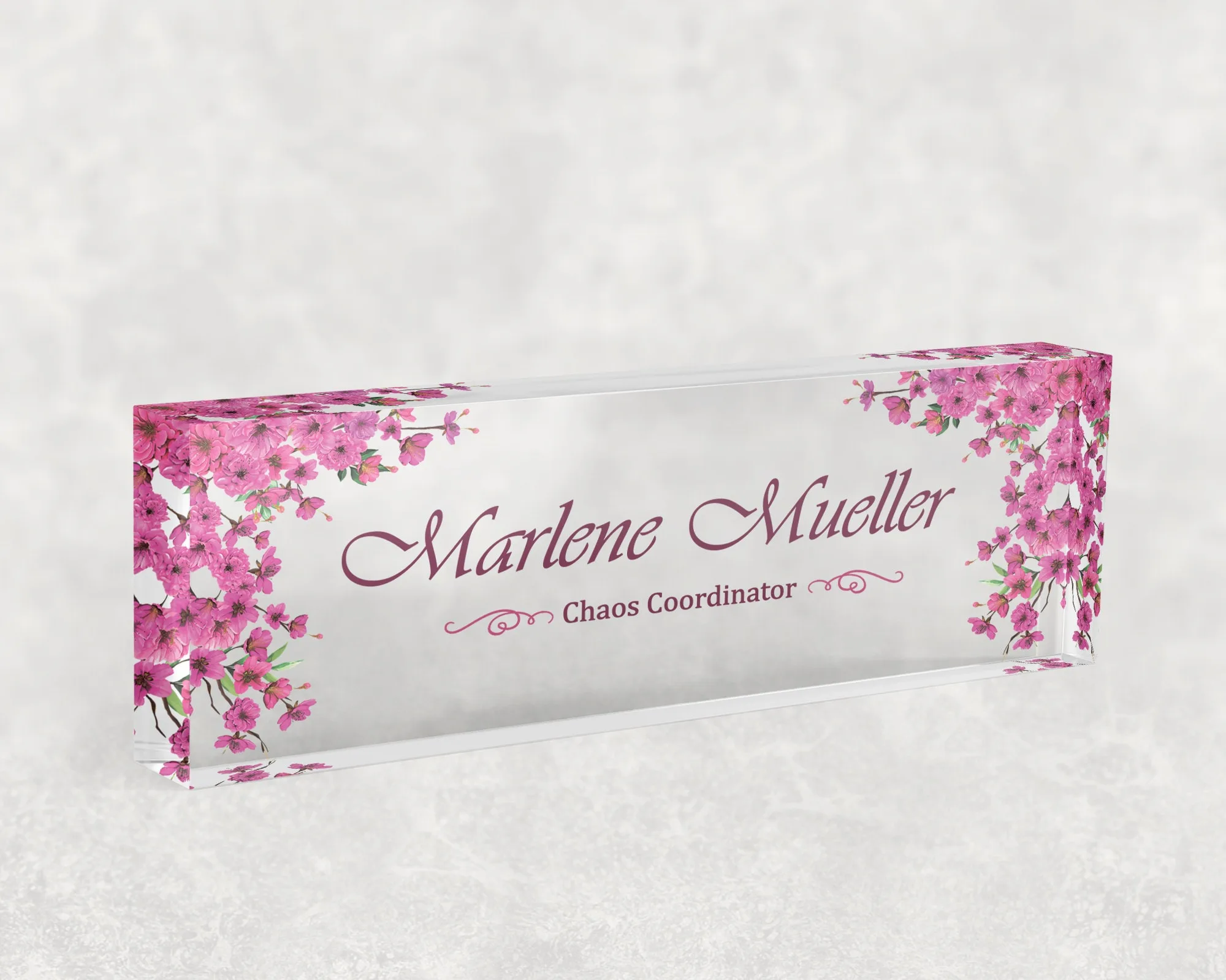 Studio view of a clear acrylic desk name plate with a pink cherry blossom design