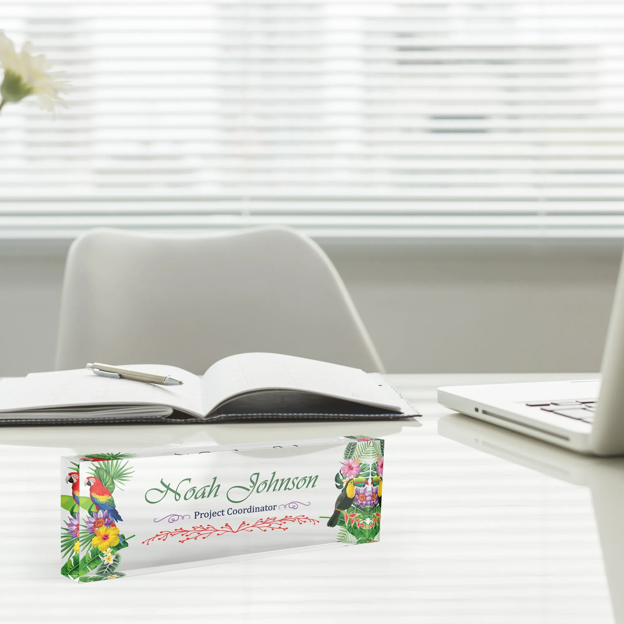 Acrylic desk name plate with a tropical parrot design beside an open notebook and a laptop