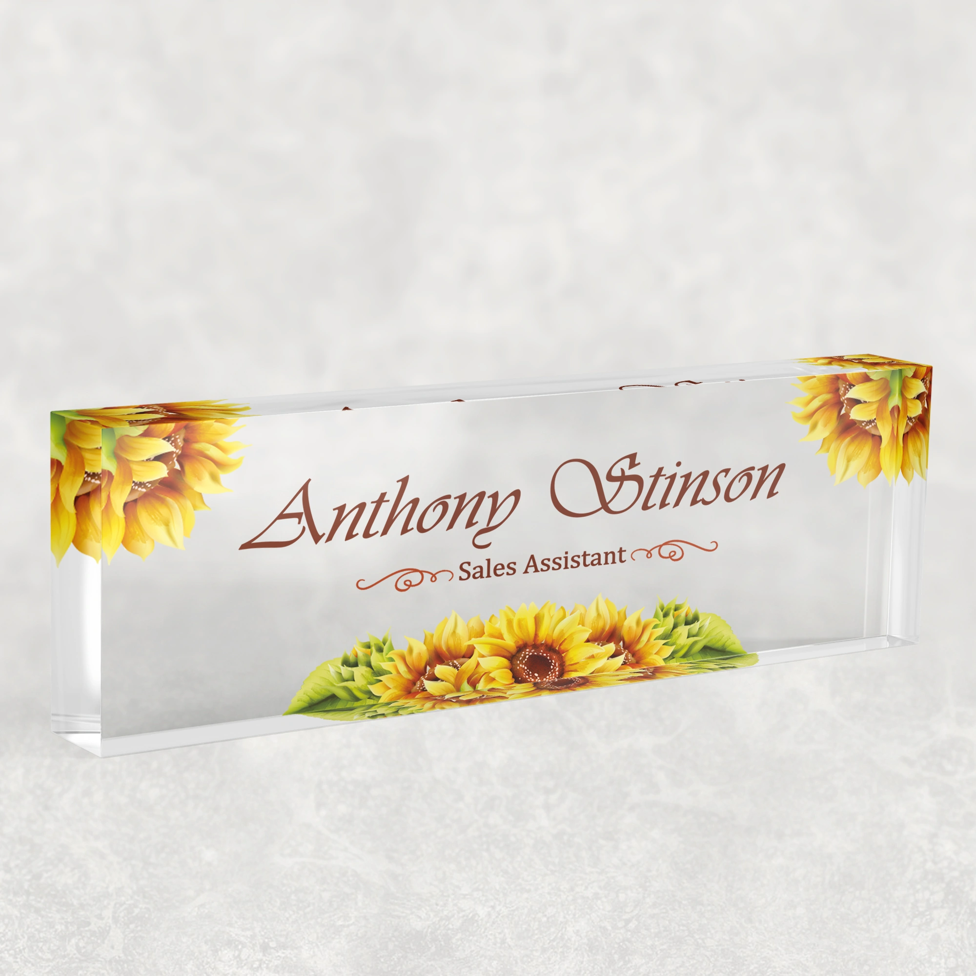 Studio view of a clear acrylic desk name plate with a yellow sunflower design