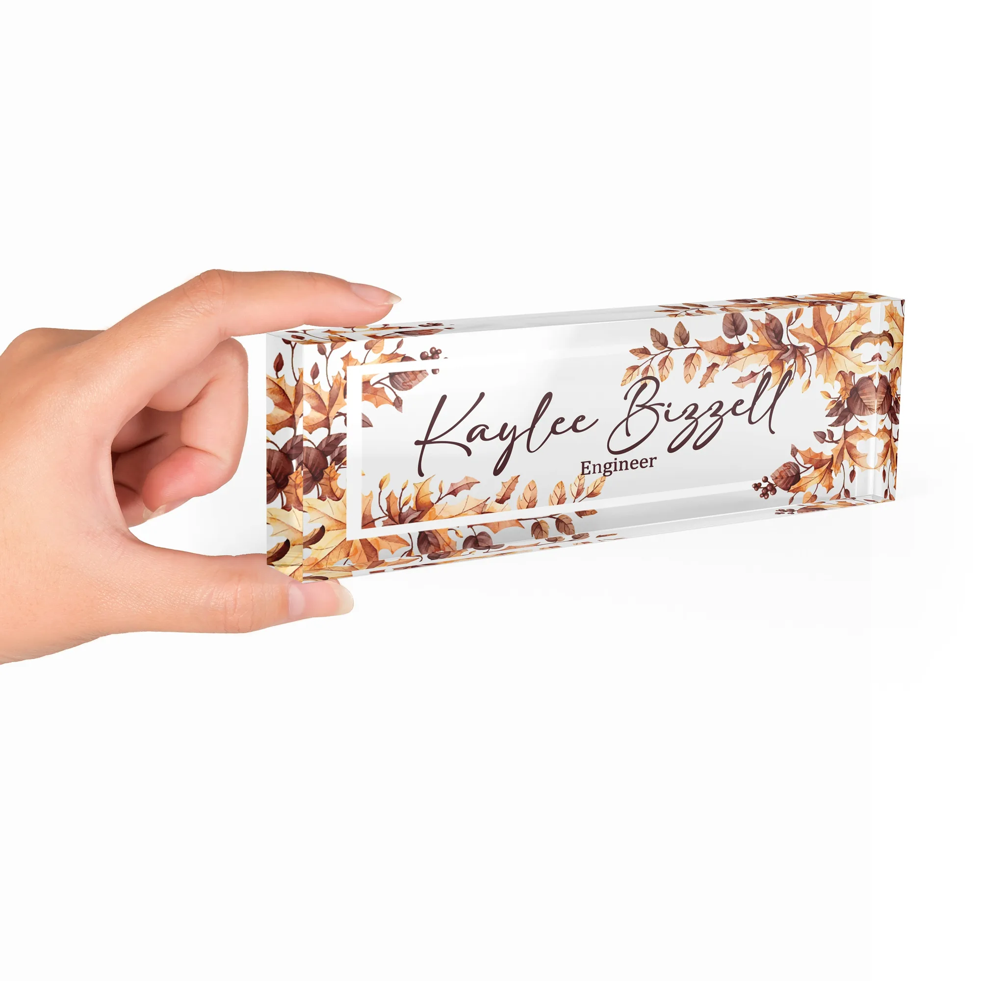 Hand holding a clear acrylic desk name plate with a golden autumn foliage design