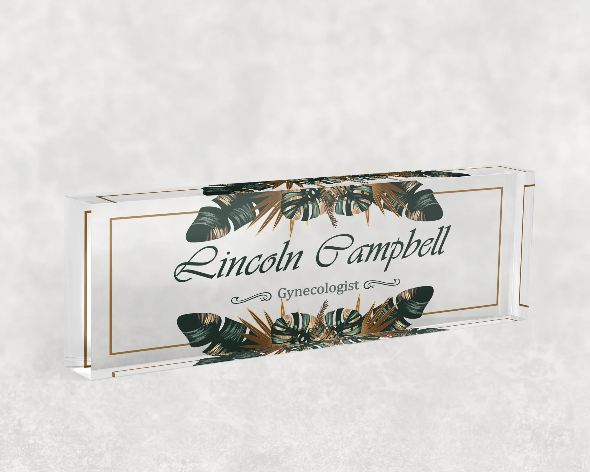 Studio view of a clear acrylic desk name plate with a green and gold tropical design