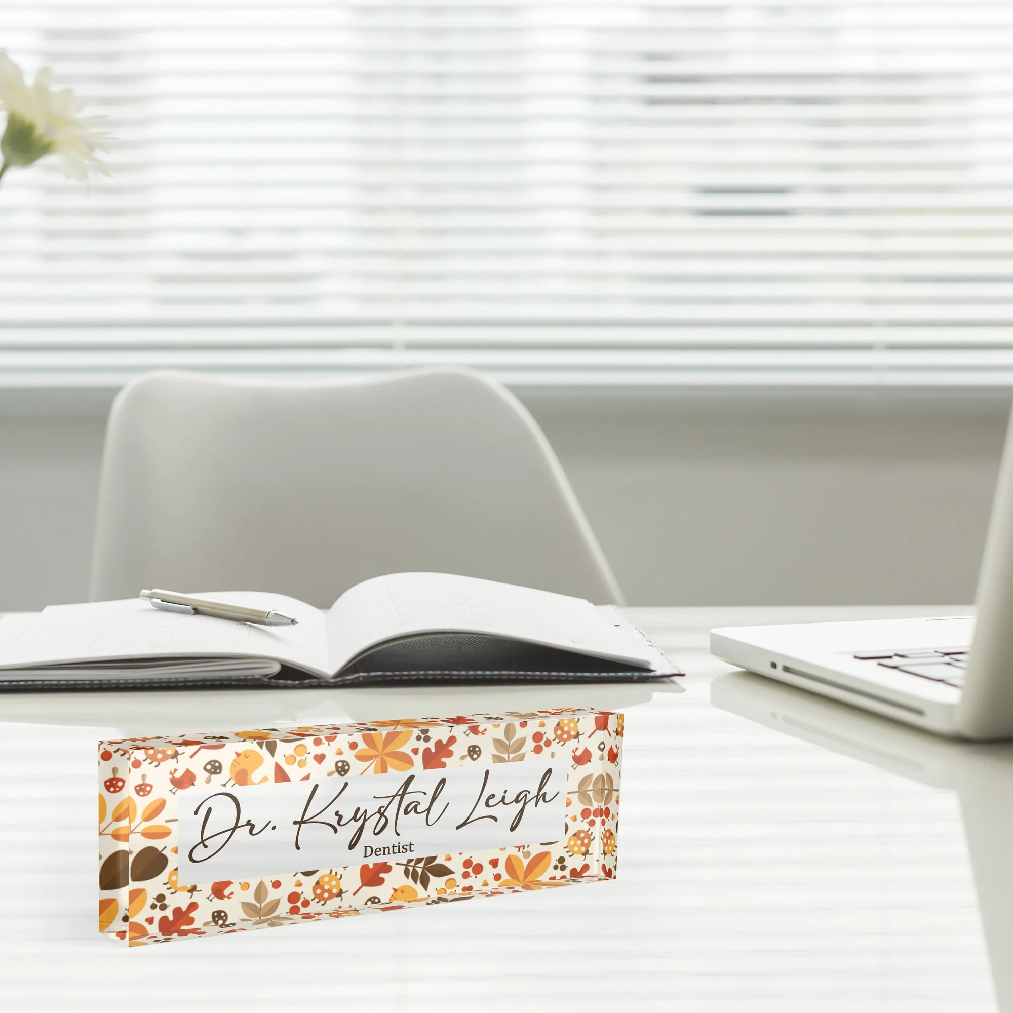 Acrylic desk name plate with an autumn leaf band design beside an open notebook and a laptop