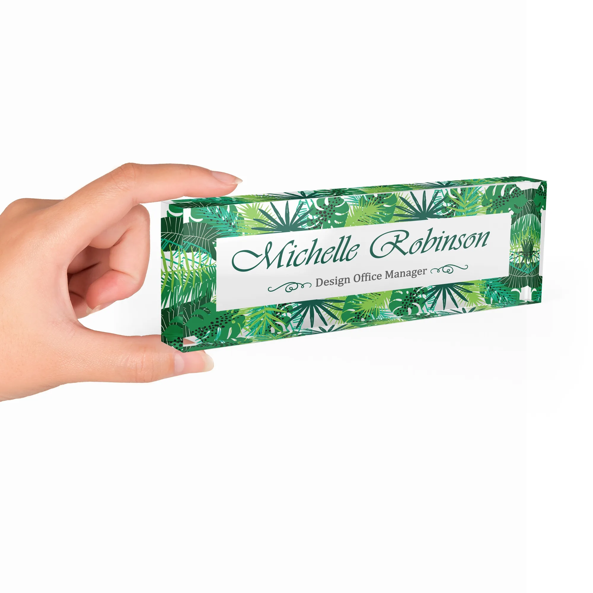 Hand holding a clear acrylic desk name plate with a deep green tropical leaf design