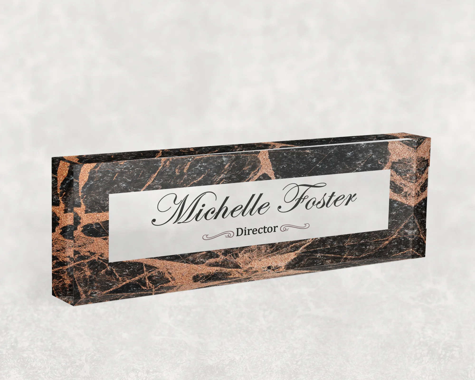 Studio view of a clear acrylic desk name plate with a black marble and copper design