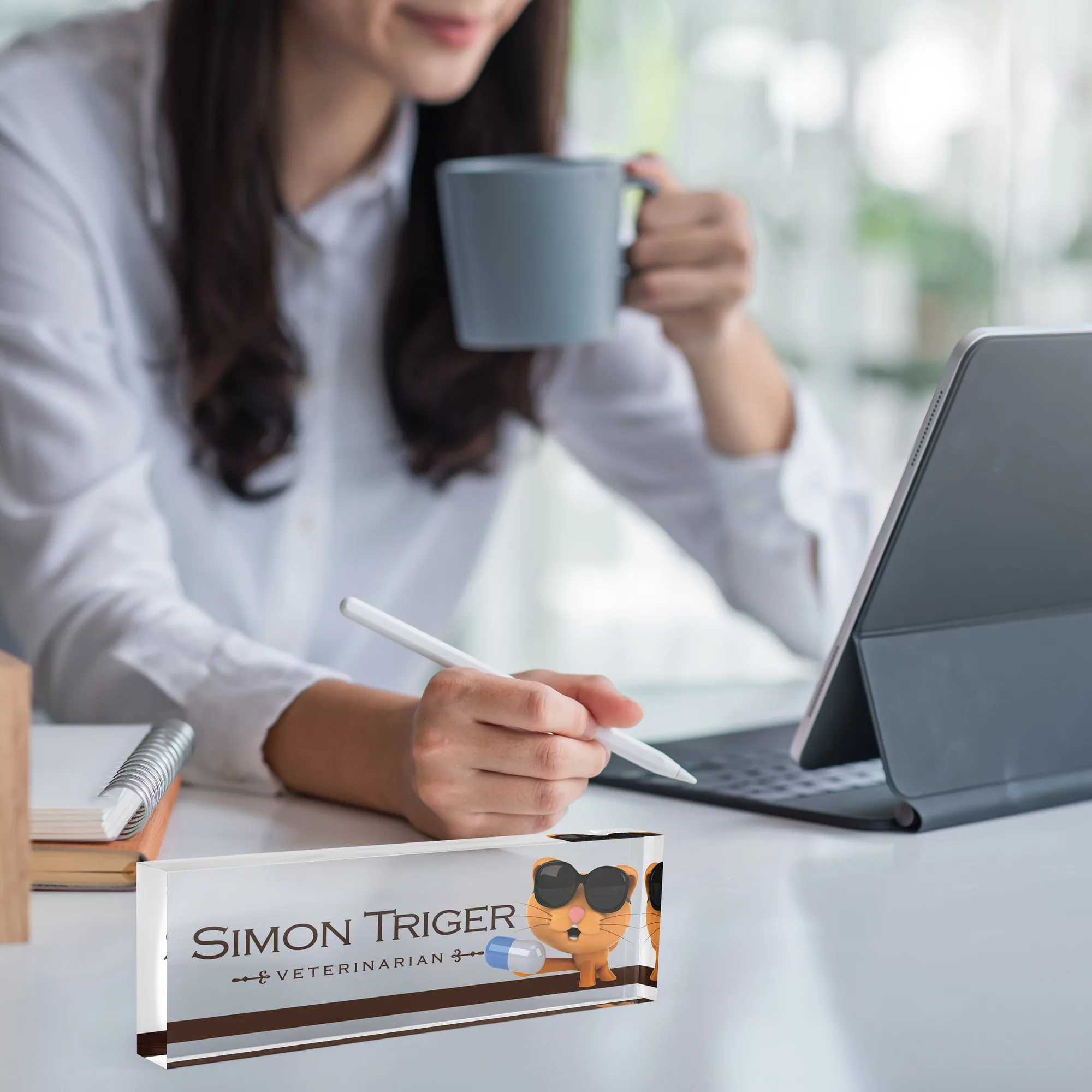 Acrylic desk name plate with a cartoon cat design on a white desk beside a tablet and a coffee mug