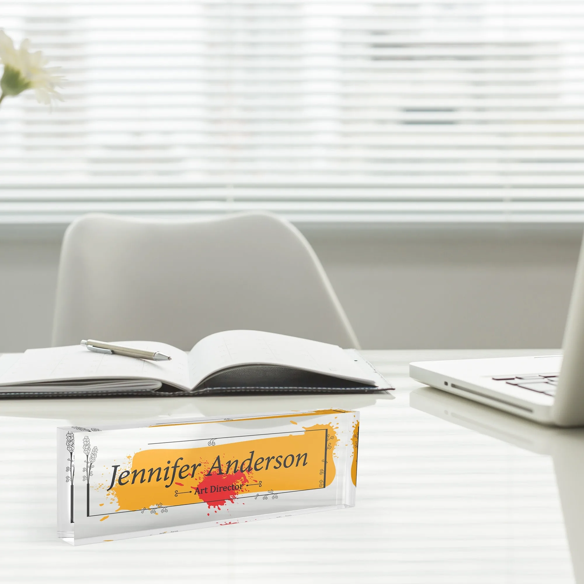 Acrylic desk name plate with a yellow brush stroke design beside an open notebook and a laptop