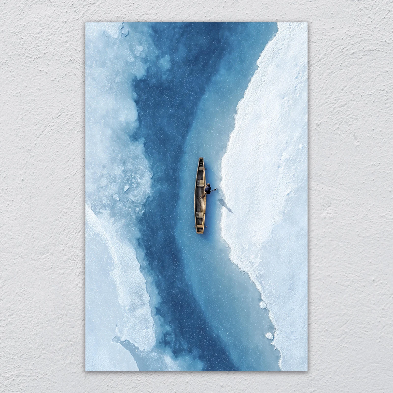 Aerial glass wall art of a lone canoe on a deep-blue frozen river between banks of white ice